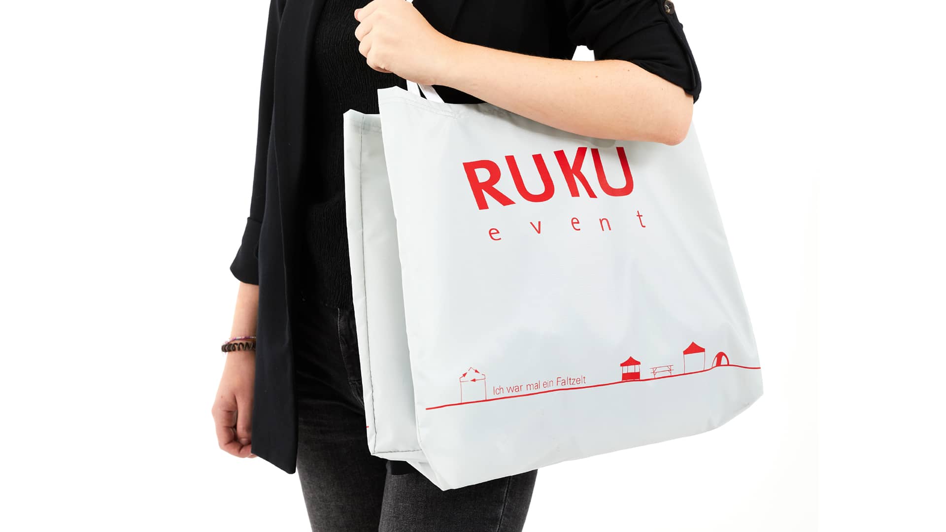 Die nachhaltige RUKUevent Einkaufstasche in der Farbe hellgrau wird von einer Person um die Schulter getragen.
