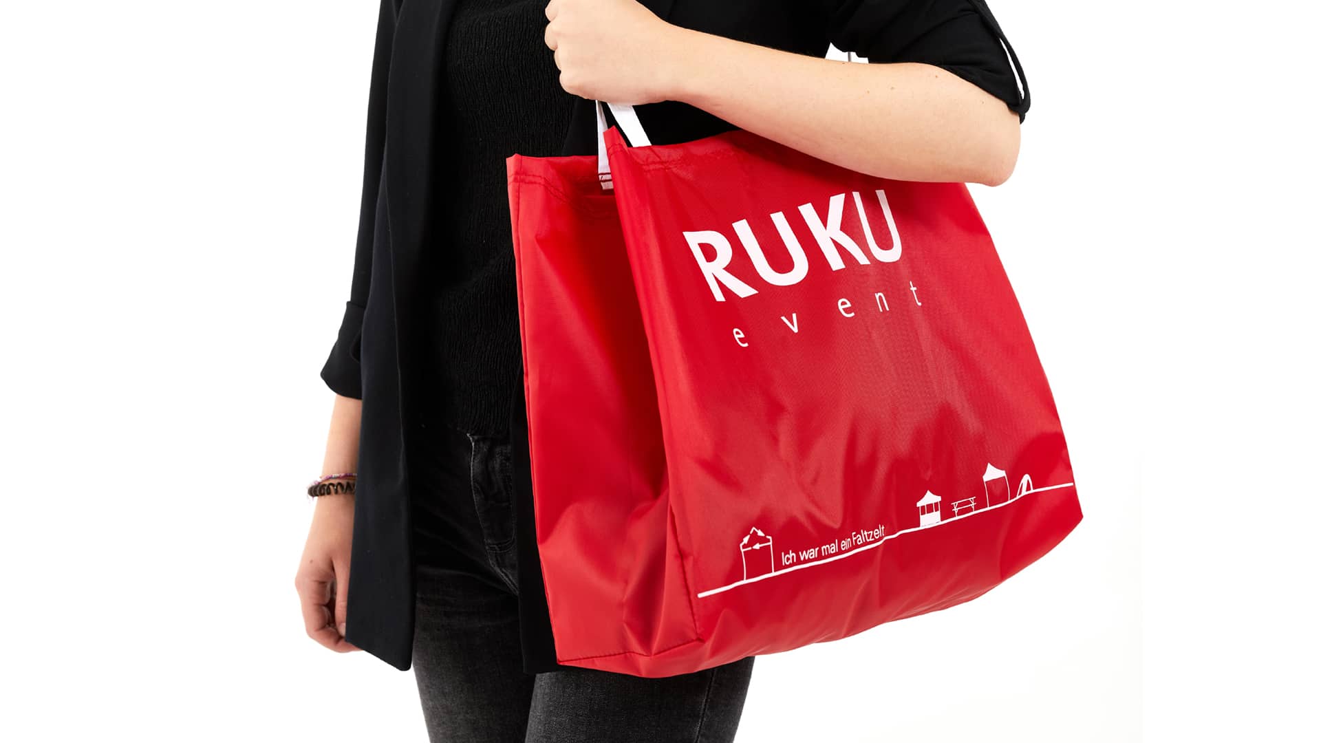 Die nachhaltige RUKUevent Einkaufstasche in der Farbe rot wird von einer Person um die Schulter getragen.