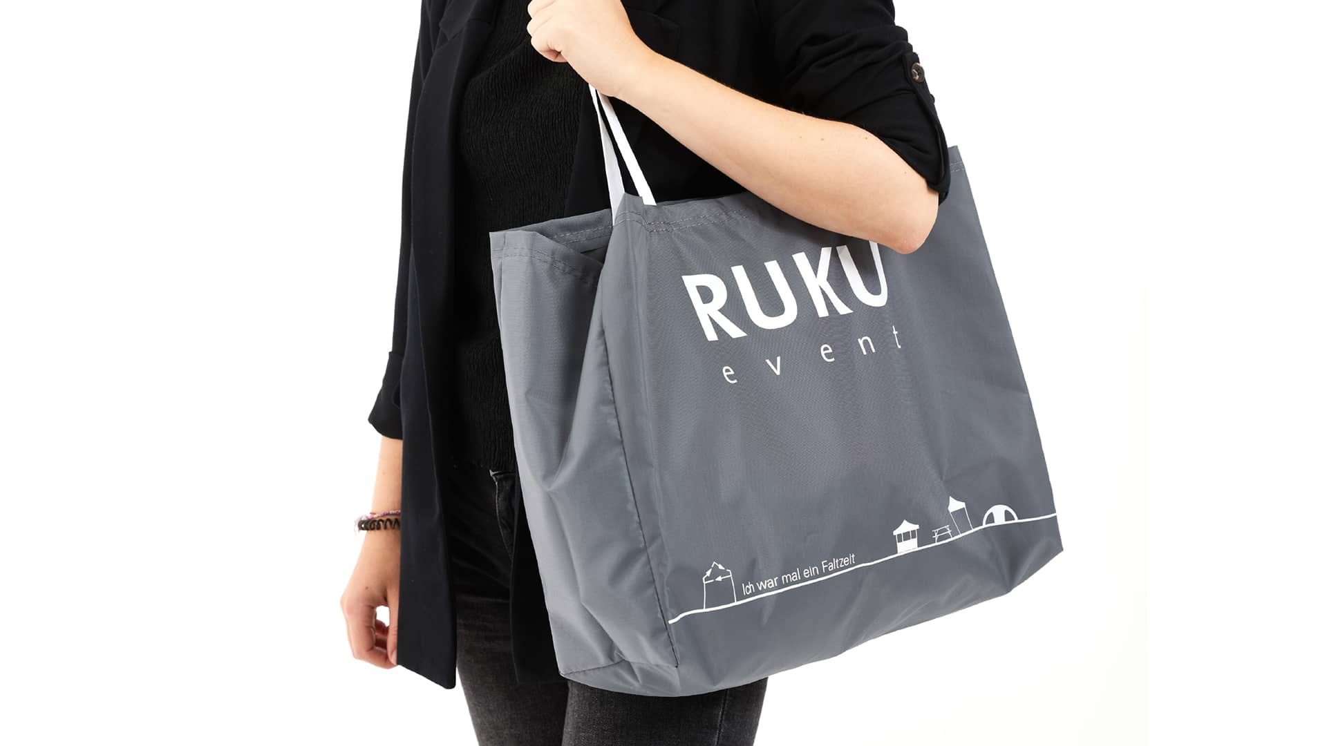 Die nachhaltige RUKUevent Einkaufstasche in der Farbe dunkelgrau wird von einer Person um die Schulter getragen.