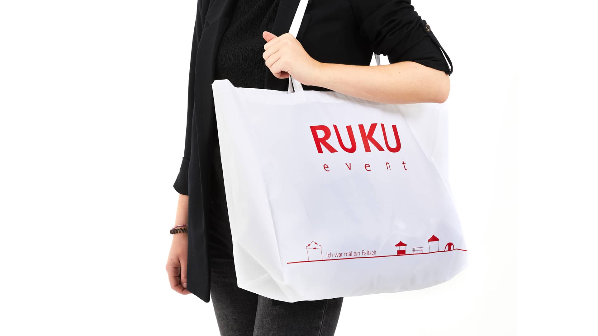 Die nachhaltige RUKUevent Einkaufstasche in der Farbe weiß wird von einer Person um die Schulter getragen.